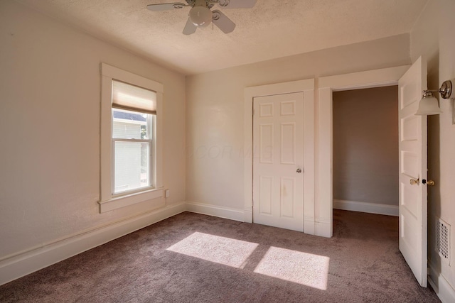 unfurnished bedroom featuring dark colored carpet, a textured ceiling, a closet, and ceiling fan