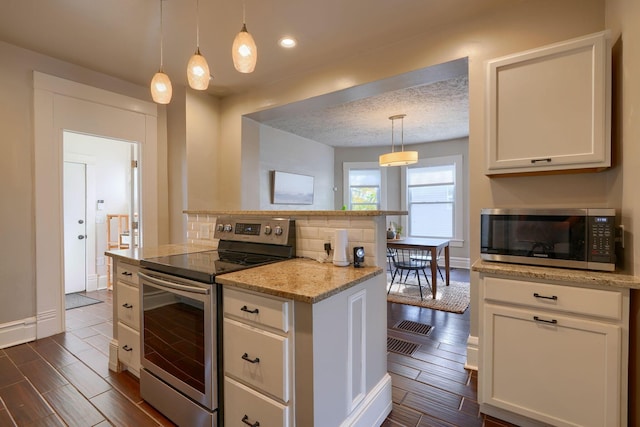 kitchen featuring dark wood-type flooring, hanging light fixtures, stainless steel appliances, and a textured ceiling