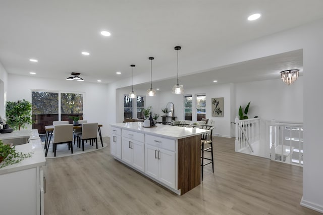 kitchen featuring white cabinetry, a center island with sink, pendant lighting, and light hardwood / wood-style floors