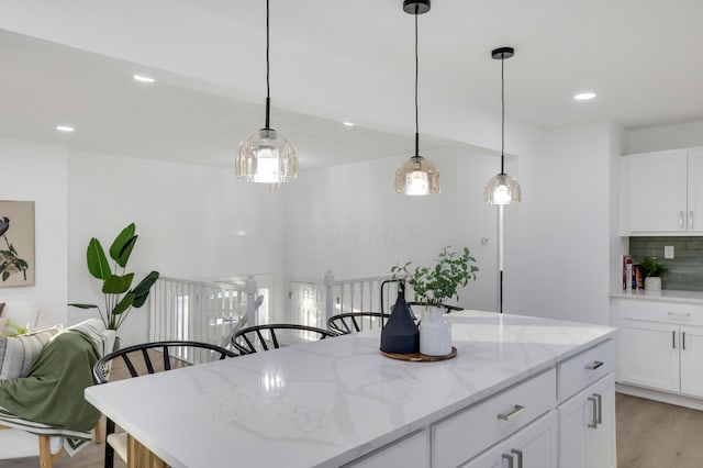 kitchen featuring white cabinetry, a center island, light stone countertops, tasteful backsplash, and light hardwood / wood-style floors