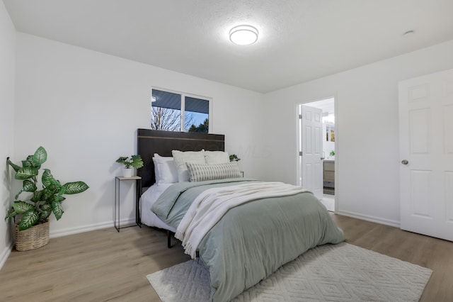 bedroom with ensuite bathroom, a textured ceiling, and light hardwood / wood-style flooring