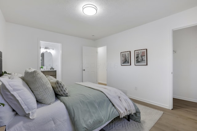 bedroom with connected bathroom, light hardwood / wood-style flooring, and a textured ceiling