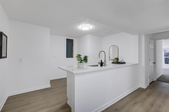 kitchen featuring kitchen peninsula, a textured ceiling, electric panel, and light hardwood / wood-style flooring