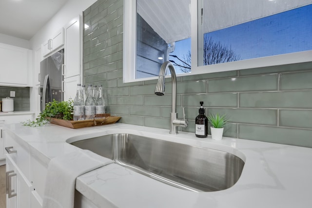 interior details featuring white cabinets, stainless steel refrigerator with ice dispenser, light stone counters, and sink