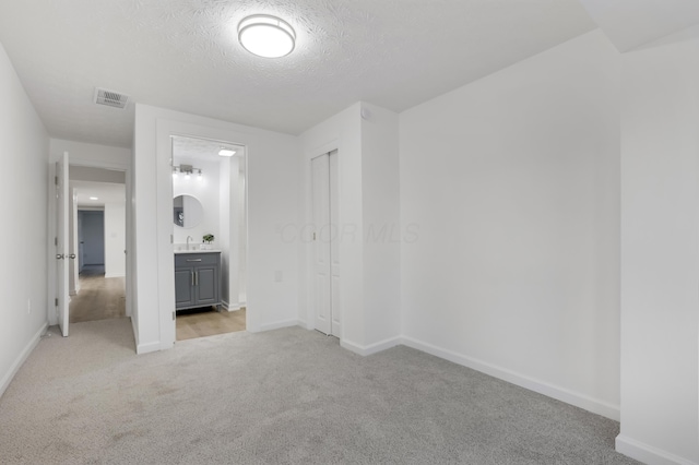 unfurnished bedroom with ensuite bath, light carpet, a closet, and a textured ceiling