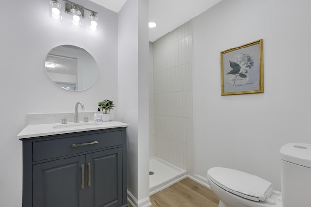 bathroom with tiled shower, vanity, hardwood / wood-style flooring, and toilet