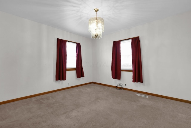 spare room featuring light carpet and an inviting chandelier