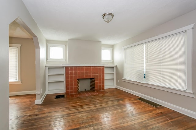 unfurnished living room featuring visible vents, plenty of natural light, hardwood / wood-style floors, and a tiled fireplace