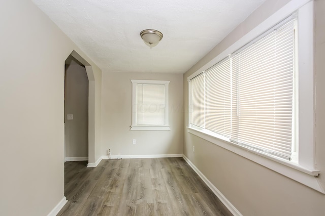 unfurnished room with baseboards, arched walkways, and wood finished floors