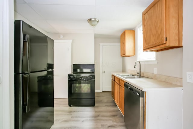 kitchen with black appliances, light countertops, light wood finished floors, and a sink