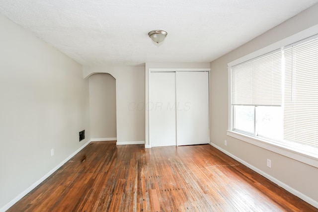 unfurnished bedroom with a closet, baseboards, arched walkways, and hardwood / wood-style flooring