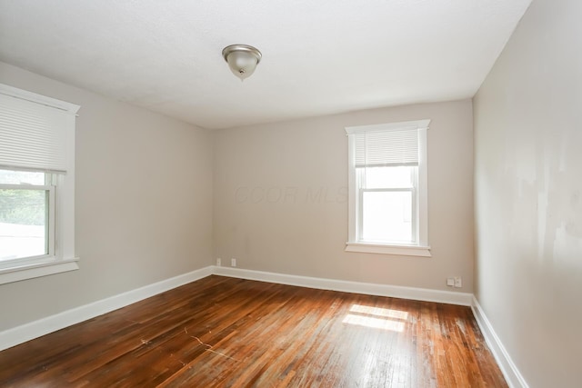 spare room featuring dark wood finished floors, plenty of natural light, and baseboards