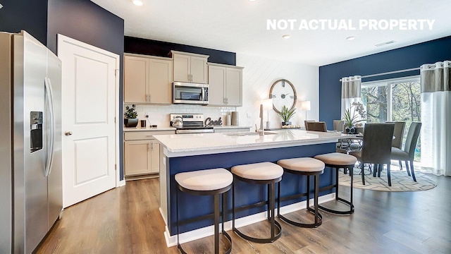 kitchen featuring a center island with sink, tasteful backsplash, appliances with stainless steel finishes, and light hardwood / wood-style flooring