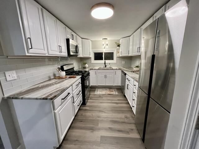 kitchen with light wood-type flooring, white cabinetry, sink, and appliances with stainless steel finishes