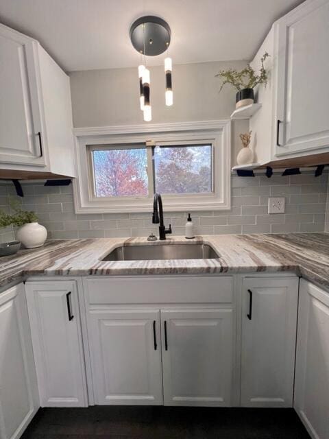 kitchen with light stone counters, white cabinetry, sink, and tasteful backsplash