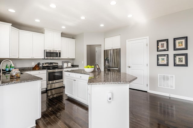 kitchen with a center island, white cabinetry, stainless steel appliances, and dark stone counters