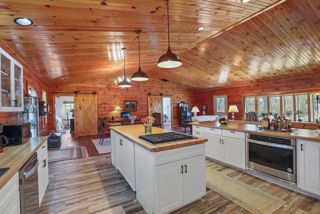 kitchen featuring stainless steel appliances, wooden walls, a barn door, white cabinets, and hanging light fixtures