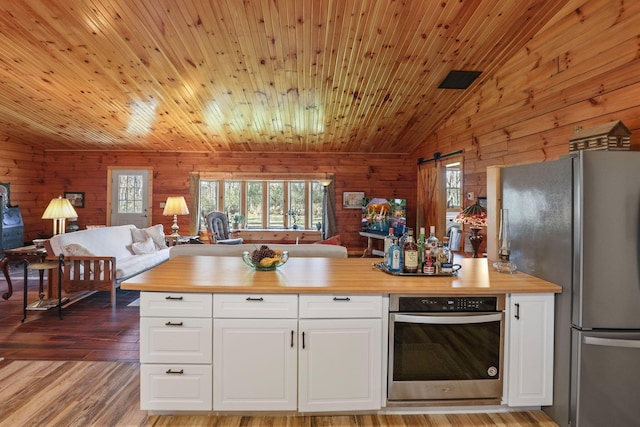 kitchen featuring butcher block countertops, stainless steel appliances, wooden walls, and vaulted ceiling