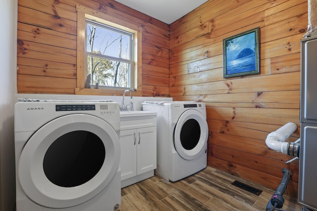 washroom featuring hardwood / wood-style floors, cabinets, sink, wooden walls, and washing machine and clothes dryer