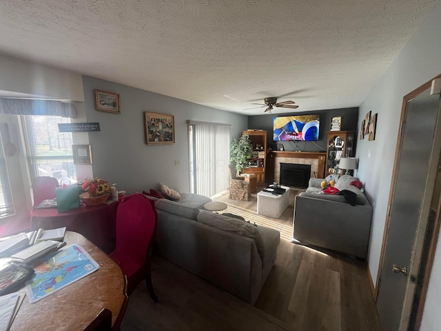 living room featuring ceiling fan, a textured ceiling, dark hardwood / wood-style floors, and a tile fireplace