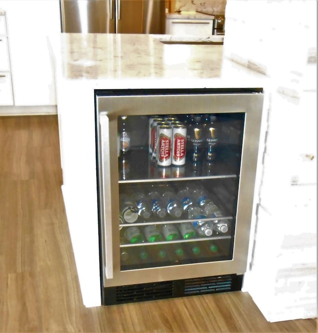 interior details featuring light stone counters, wood-type flooring, beverage cooler, and stainless steel refrigerator