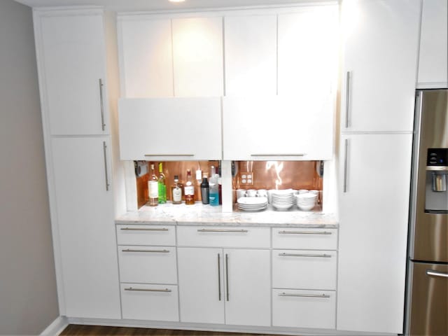 bar with dark hardwood / wood-style flooring, white cabinetry, light stone counters, and stainless steel fridge with ice dispenser