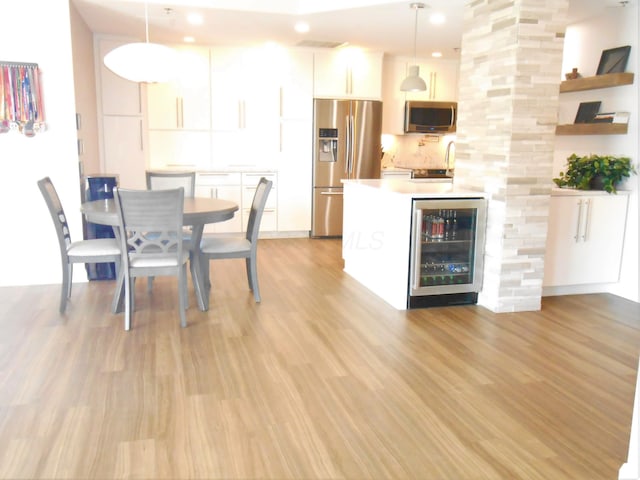 kitchen with white cabinets, stainless steel appliances, light hardwood / wood-style flooring, and hanging light fixtures