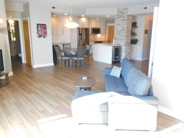 living room with wine cooler, sink, light hardwood / wood-style floors, and ornate columns