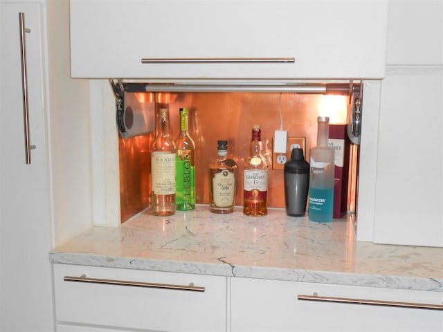 bar with white cabinets and light stone countertops