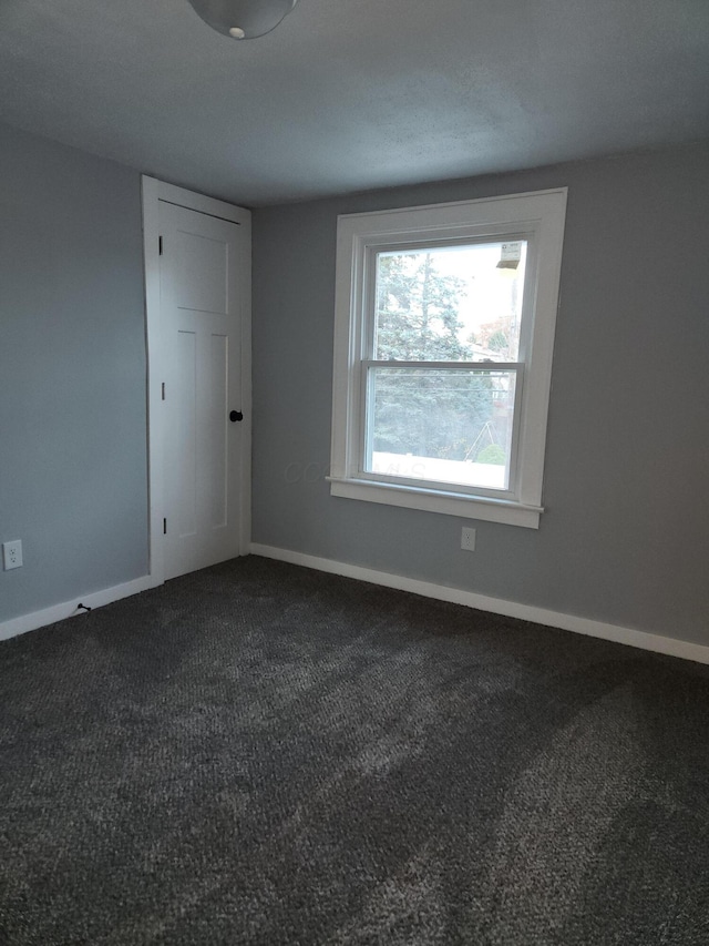 spare room with baseboards and dark colored carpet