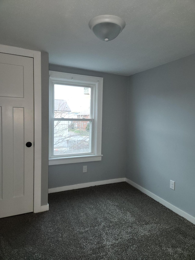 empty room featuring dark carpet and baseboards