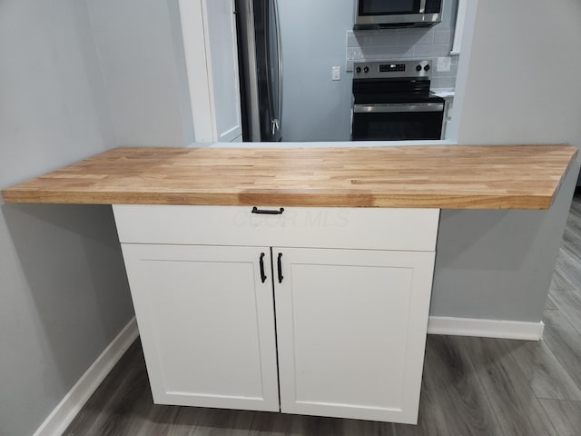 kitchen featuring butcher block countertops, tasteful backsplash, appliances with stainless steel finishes, and dark wood finished floors