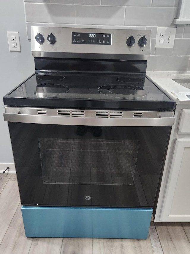 interior details featuring backsplash, stainless steel electric stove, light countertops, light wood-style flooring, and white cabinets