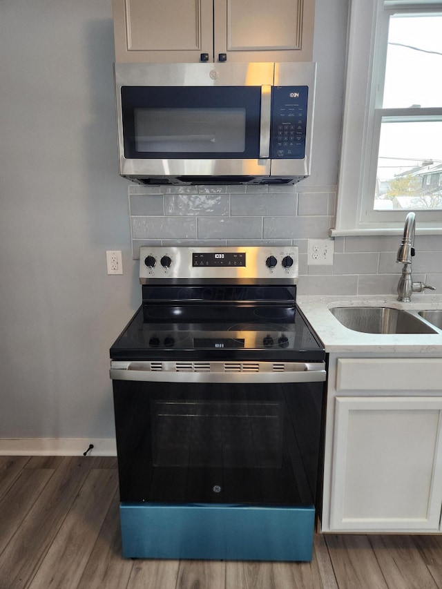 kitchen featuring wood finished floors, a sink, stainless steel appliances, white cabinets, and tasteful backsplash