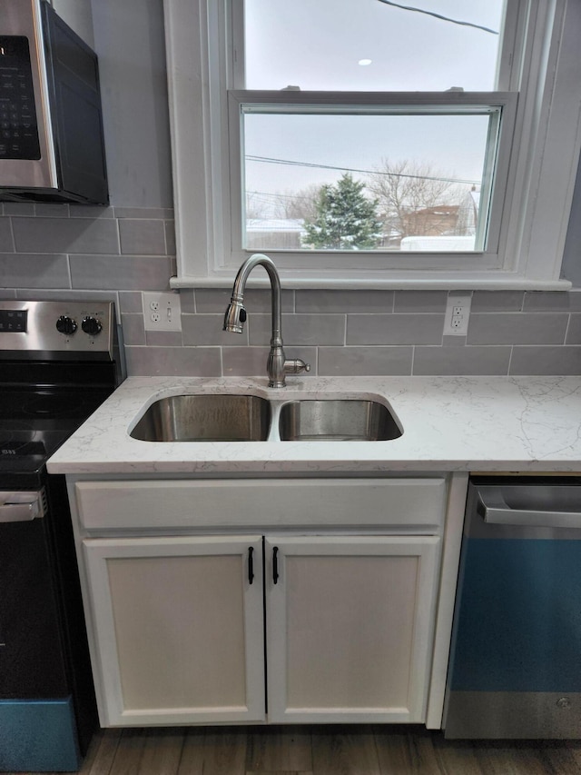 kitchen with light stone countertops, a sink, stainless steel appliances, white cabinetry, and tasteful backsplash