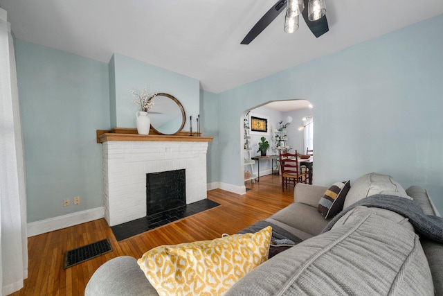 living room with ceiling fan, hardwood / wood-style floors, and a brick fireplace