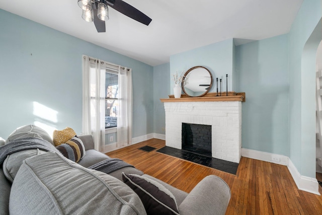 living room with ceiling fan, dark wood-type flooring, and a brick fireplace