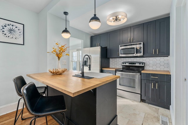 kitchen featuring decorative light fixtures, backsplash, stainless steel appliances, and butcher block counters