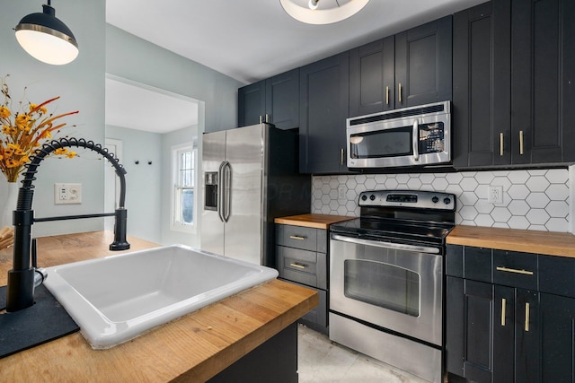 kitchen with appliances with stainless steel finishes, butcher block countertops, tasteful backsplash, and sink