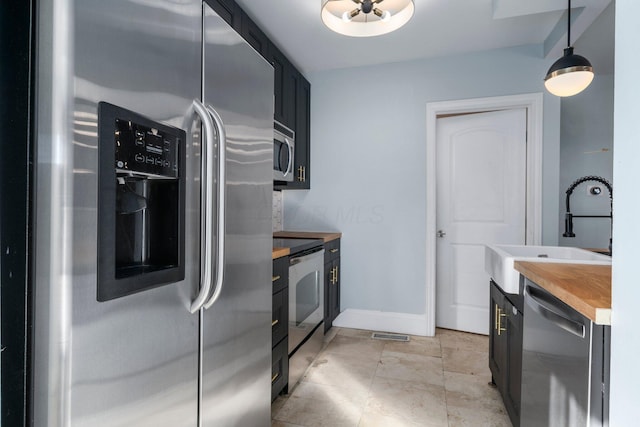 kitchen featuring butcher block countertops, decorative light fixtures, sink, and appliances with stainless steel finishes