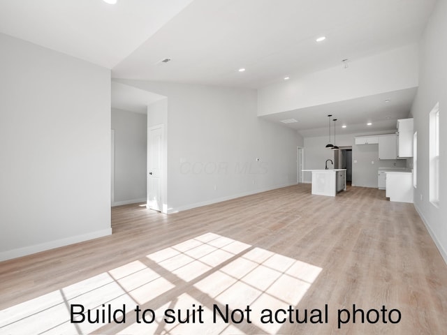 unfurnished living room with vaulted ceiling, light hardwood / wood-style flooring, and sink