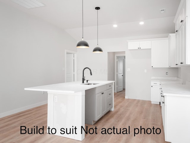 kitchen featuring white cabinets, light hardwood / wood-style flooring, an island with sink, and hanging light fixtures