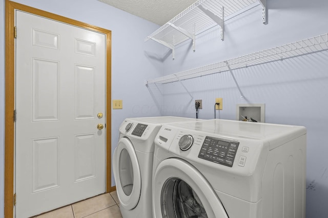 clothes washing area with independent washer and dryer, a textured ceiling, and light tile patterned floors