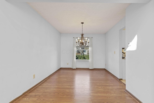 unfurnished dining area featuring a notable chandelier, a textured ceiling, and light hardwood / wood-style flooring