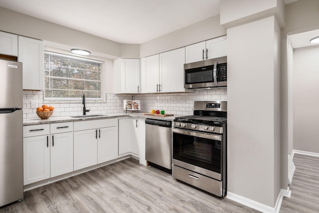 kitchen with white cabinets, sink, light stone countertops, light wood-type flooring, and stainless steel appliances