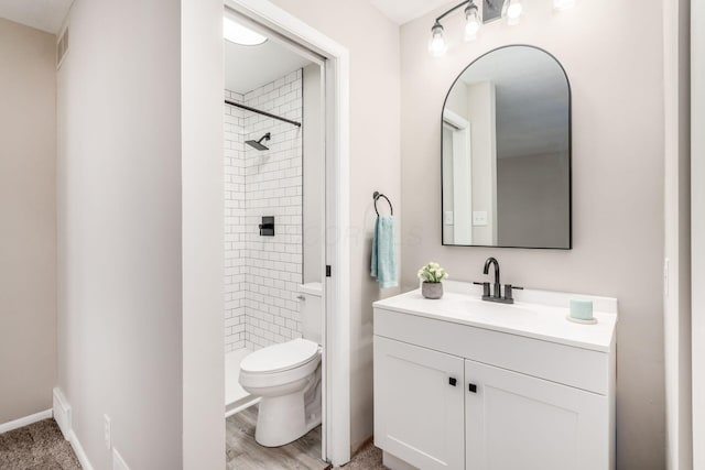 bathroom featuring hardwood / wood-style flooring, toilet, vanity, and tiled shower