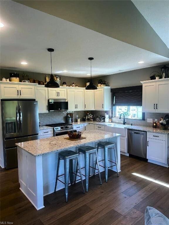 kitchen with white cabinets, decorative light fixtures, a center island, and appliances with stainless steel finishes