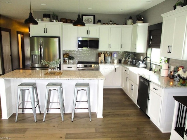 kitchen featuring appliances with stainless steel finishes, dark hardwood / wood-style flooring, pendant lighting, white cabinets, and a kitchen island