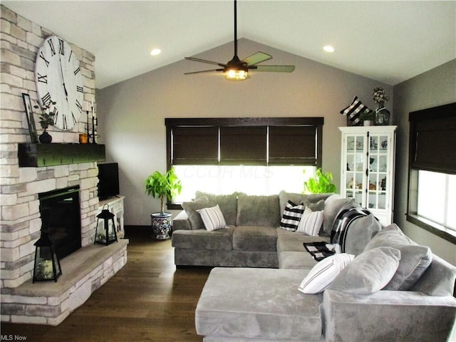 living room with dark hardwood / wood-style flooring, a stone fireplace, a wealth of natural light, and lofted ceiling