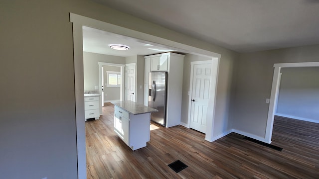 kitchen with a center island, stainless steel refrigerator with ice dispenser, dark hardwood / wood-style floors, light stone counters, and white cabinetry